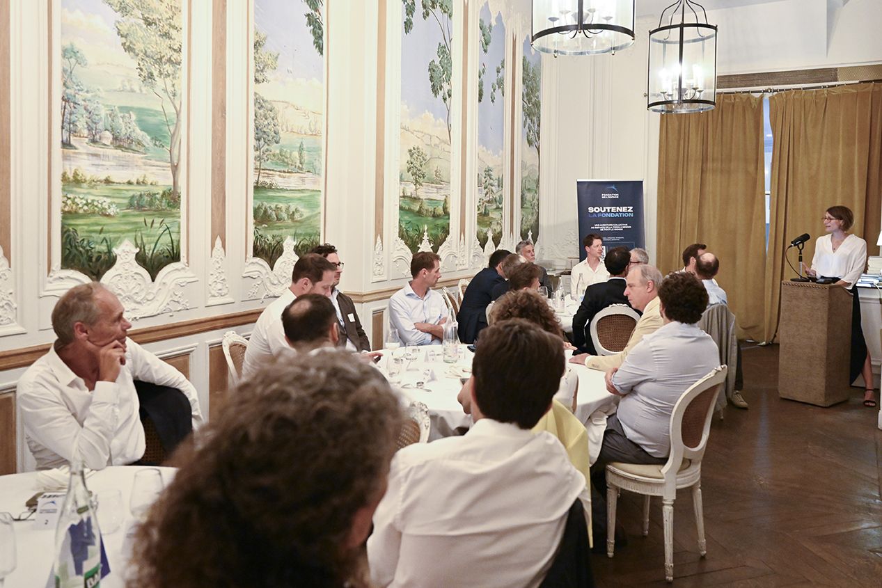 Vue large du salon aux panneaux peints, convives attablés et intervenante au pupitre